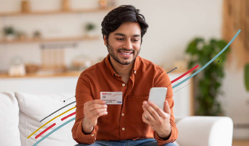a man looking at his phone and holding a Tech CU credit card
